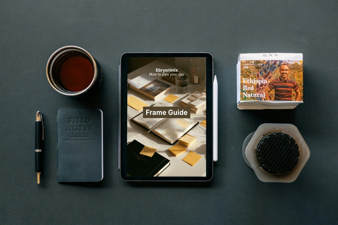 Tablet displaying a coffee-themed app, coffee cup, notebook, pen, and coffee package on a dark surface.